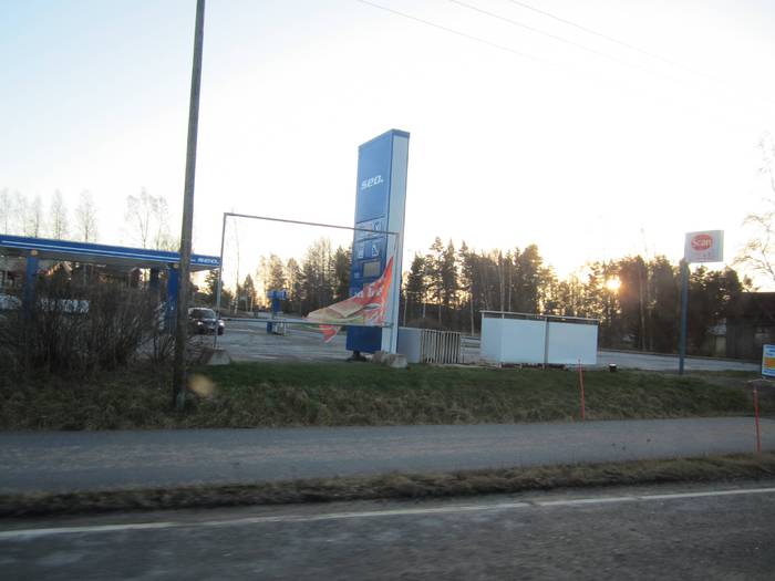Bensa-asema pimeänä ja mainos revennyt.